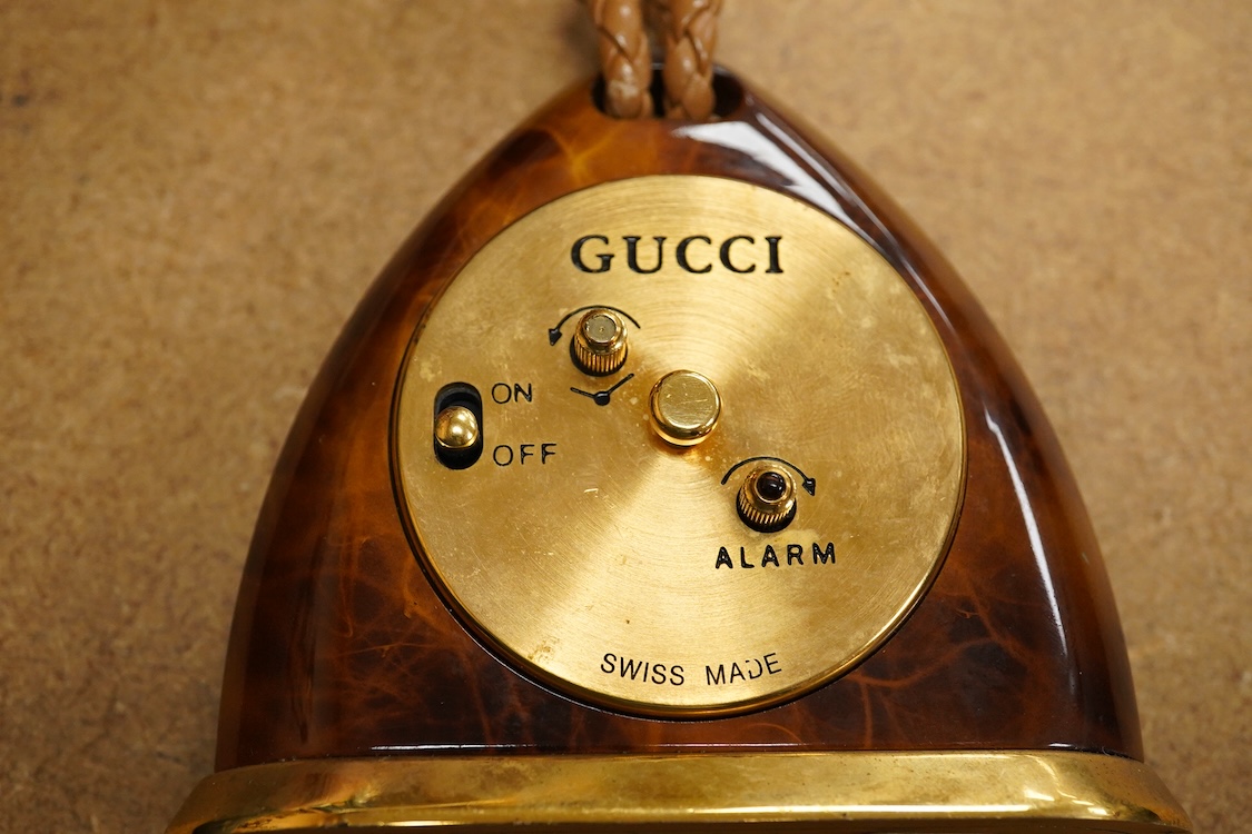 A Gucci gilt and enamelled stirrup shaped alarm clock with plaited and tasselled leather decoration, 9cm high
